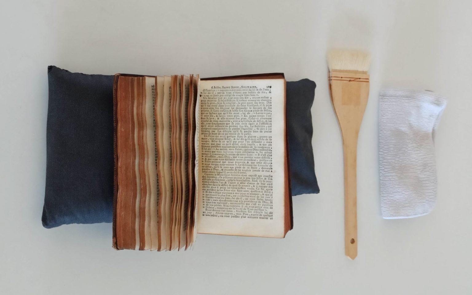 Livro antigo ao lado de escova Hake e pano de microfibras branco